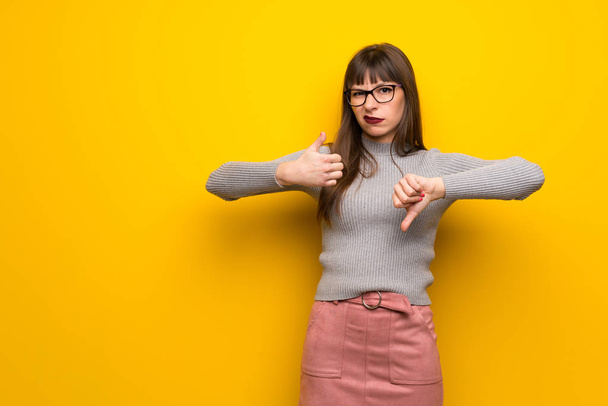 Femme avec des lunettes sur le mur jaune faisant signe bon-mauvais. Indécis entre oui et non
 - Photo, image