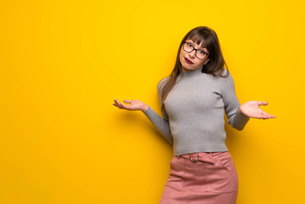 Жінка в окулярах над жовтою стіною має сумніви під час підняття рук і плечей
 - Фото, зображення