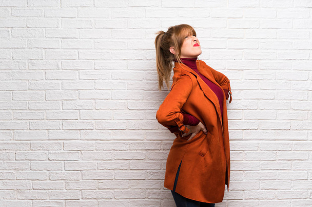 Femme avec manteau sur mur de briques blanches souffrant de maux de dos pour avoir fait un effort
 - Photo, image