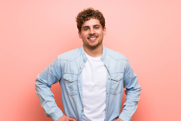 Homme blond sur un mur rose posant avec les bras à la hanche et riant en regardant vers l'avant
 - Photo, image
