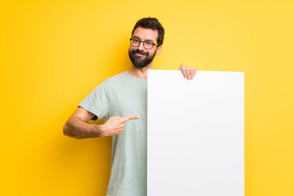 Mann mit Bart und grünem Hemd hält ein leeres Plakat in der Hand, um ein Konzept einzufügen - Foto, Bild