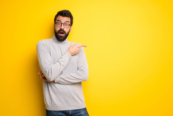 Man with beard and turtleneck surprised and pointing side - Foto, Bild