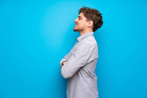 Blonde man over blue wall in lateral position - Foto, afbeelding