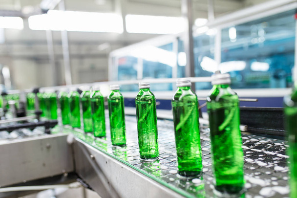 瓶詰めプラント - 処理し、緑のガラスボトルに純粋な泉の水を瓶詰めするための水瓶詰めライン。選択フォーカス.  - 写真・画像