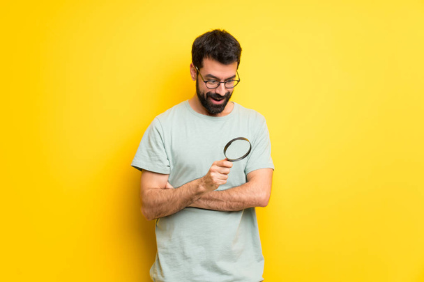 Man with beard and green shirt holding a magnifying glass - Foto, immagini