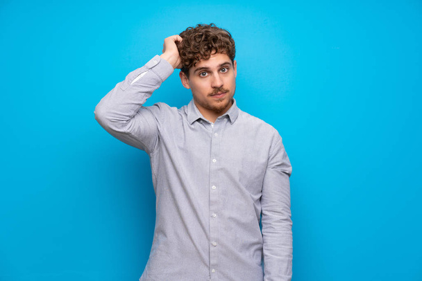 Blonde man over blue wall with an expression of frustration and not understanding - Photo, Image
