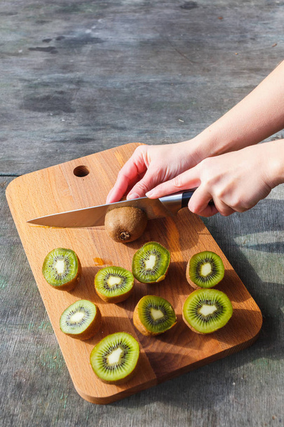 Female hands cut kiwi on a cutting board on gray vintage background - Foto, afbeelding