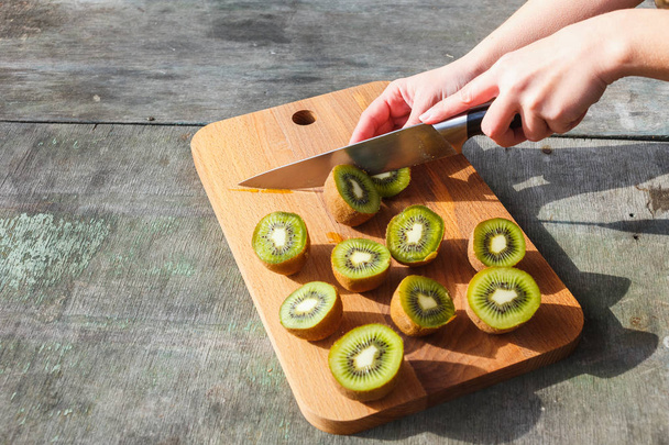 Female hands cut kiwi on a cutting board on gray vintage background - Photo, image