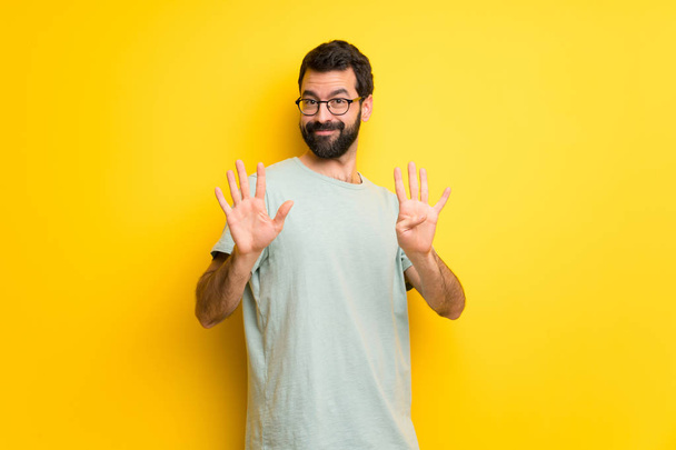 Mann mit Bart und grünem Hemd zählt neun mit den Fingern - Foto, Bild