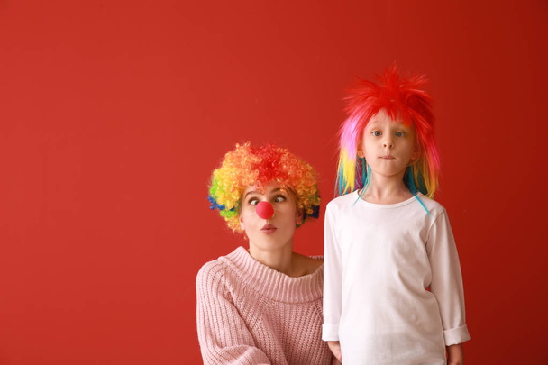 Woman and little girl in funny disguise on color background. April fools' day celebration - Photo, Image