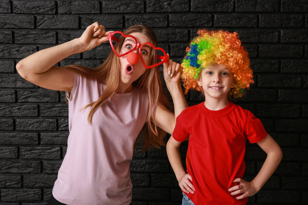Frau und kleines Mädchen in lustiger Verkleidung auf dunklem Hintergrund. Aprilscherz-Fest - Foto, Bild