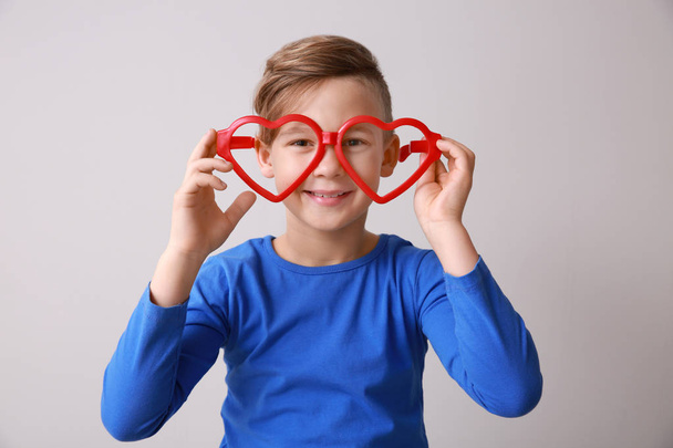 Funny little boy with big heart-shaped glasses on light background - Foto, immagini
