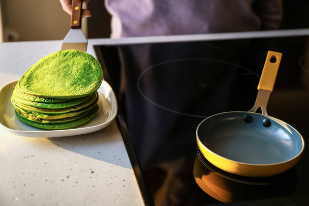 Woman putting freshly fried green pancakes onto plate in kitchen - Photo, image