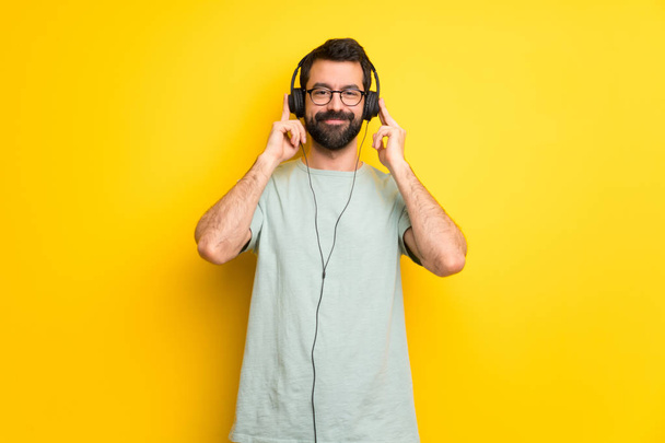 Mies, jolla on parta ja vihreä paita kuuntelemassa musiikkia kuulokkeilla
 - Valokuva, kuva