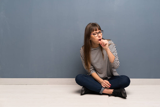 Γυναίκα με τα γυαλιά, κάθεται στο πάτωμα είναι που υποφέρουν με βήχα και αίσθημα κακή - Φωτογραφία, εικόνα