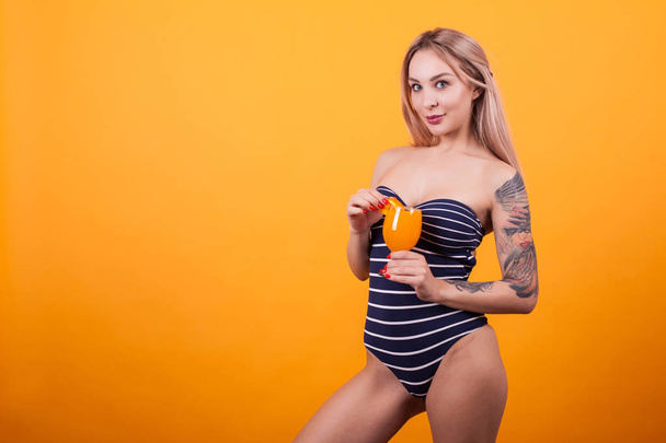 Mooie jonge vrouw met tatto op haar armn lekker drankje houden over gele achtergrond - Foto, afbeelding