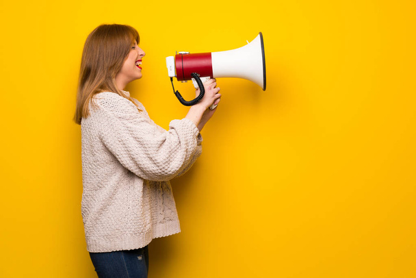 Рыжая женщина на желтой стене кричит через мегафон
 - Фото, изображение