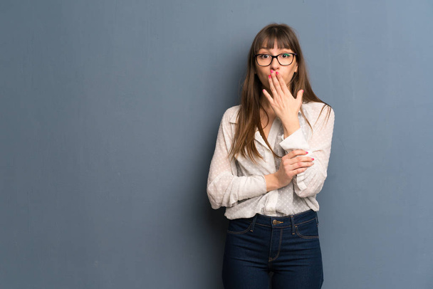 Woman with glasses over blue wall covering mouth with hands for saying something inappropriate - Photo, Image