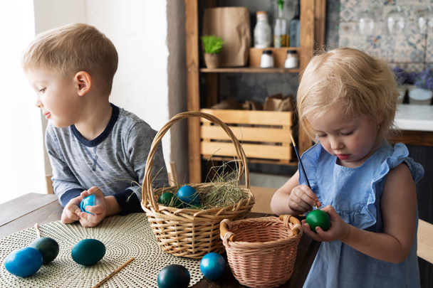 Húsvéti ünnepek: gyermek lány és fiú, festeni a tojásokat egy ecsettel a konyhában. - Fotó, kép