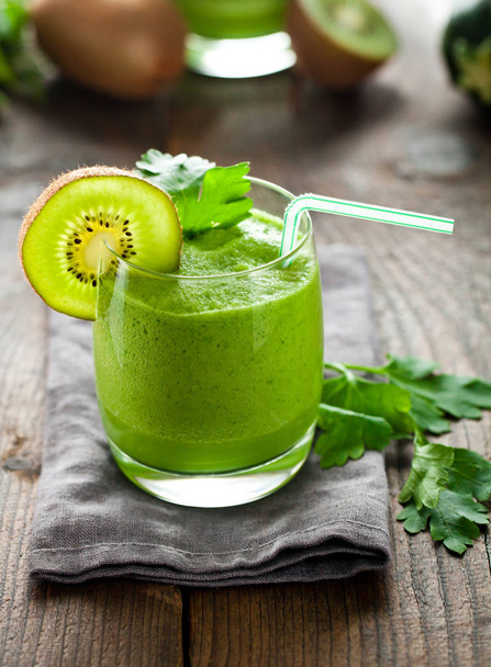 close-up view of glass with kiwi smoothie, parsley and drinking straw on wooden table - Photo, image