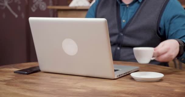 Male freelancer sips coffee while working from a small coffee shop. - Filmati, video