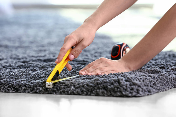 Woman with tape measure cutting carpet on floor - Фото, зображення