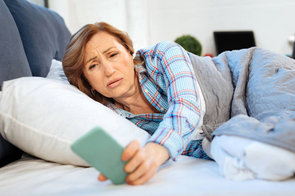 Upset mature woman taking smartphone from nightstand and checking time - Foto, immagini