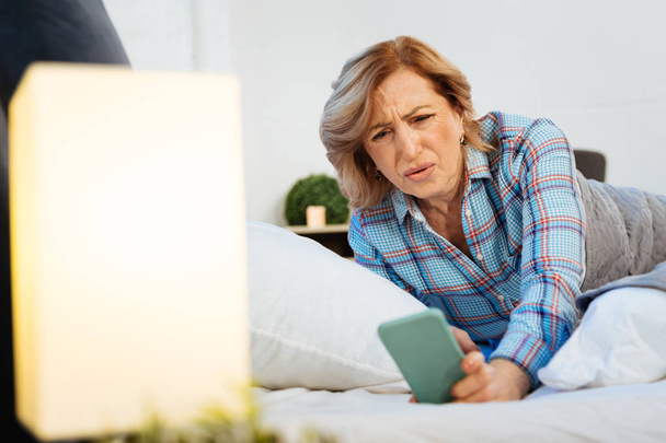 Confused short-haired adult woman in bright pajama looking on screen - Photo, image