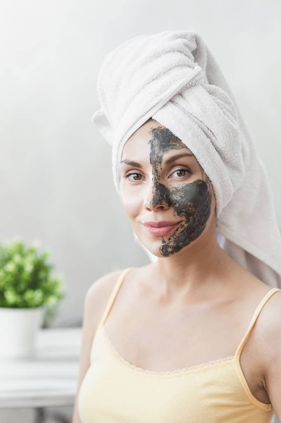 Face Skin care. Attractive Young Woman Wrapped in Bath Towel, applying clay mud mask to face. Skin care concept. Girl taking care of complexion. Beauty treatments - Foto, Bild