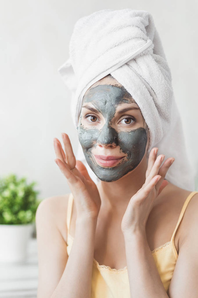 Face Skin care. Attractive Young Woman Wrapped in Bath Towel, applying clay mud mask to face. Skin care concept. Girl taking care of complexion. Beauty treatments - Foto, Imagen