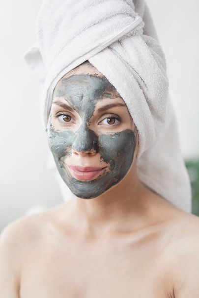 Face Skin care. Attractive Young Woman Wrapped in Bath Towel, applying clay mud mask to face. Skin care concept. Girl taking care of complexion. Beauty treatments - Foto, afbeelding