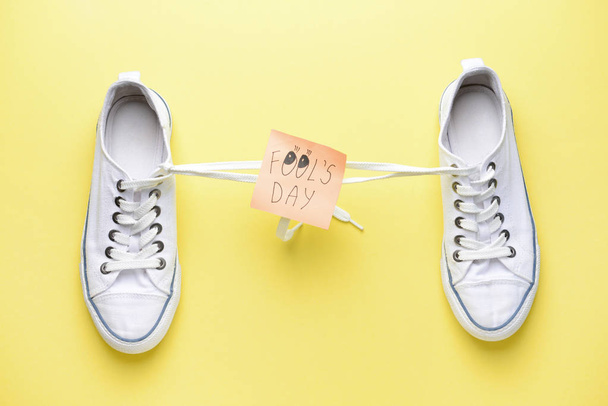 Chaussures avec lacets attachés ensemble et note collante avec texte FOOL'S DAY sur fond de couleur
 - Photo, image