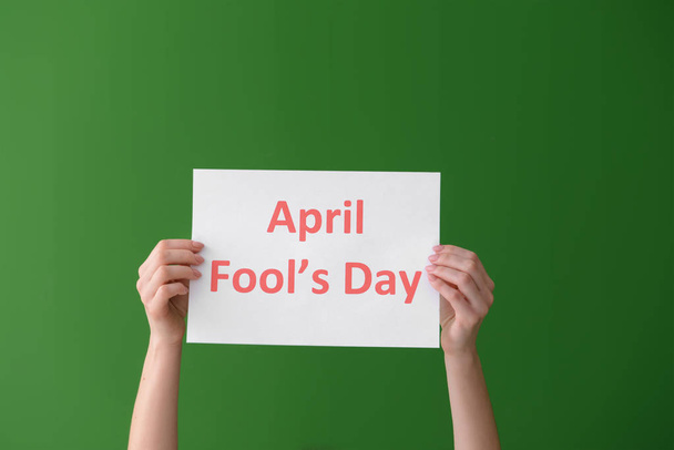 Female hands holding paper sheet with text APRIL FOOL'S DAY on color background - Photo, Image