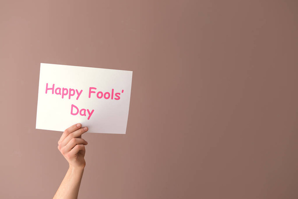 Male hand holding paper sheet with text HAPPY FOOL'S DAY on color background - Photo, image