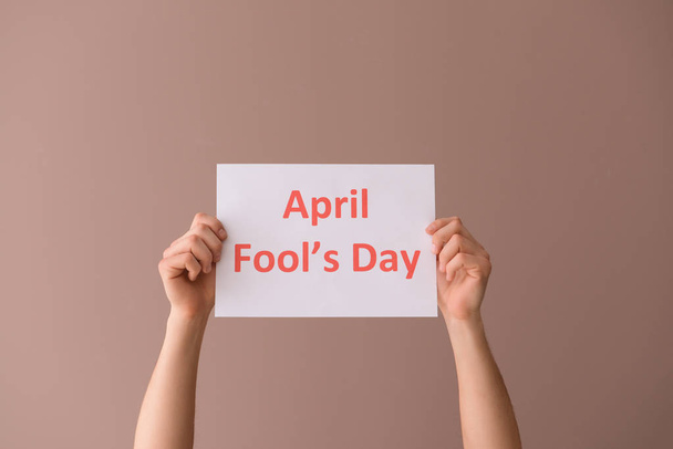 Male hands holding paper sheet with text APRIL FOOL'S DAY on color background - Photo, Image