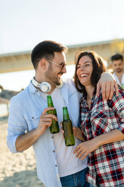 Happy young couple smiling and drinking beer at beach - Фото, зображення