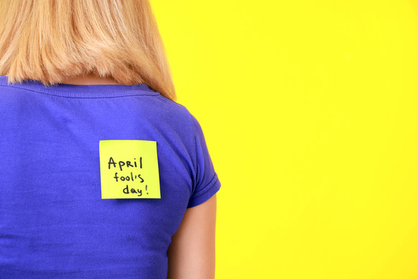 Sticky note with text APRIL FOOLS DAY on back of beautiful woman against color background - Zdjęcie, obraz