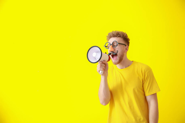 Funny man with megaphone on color background. April Fools' Day prank - Foto, immagini