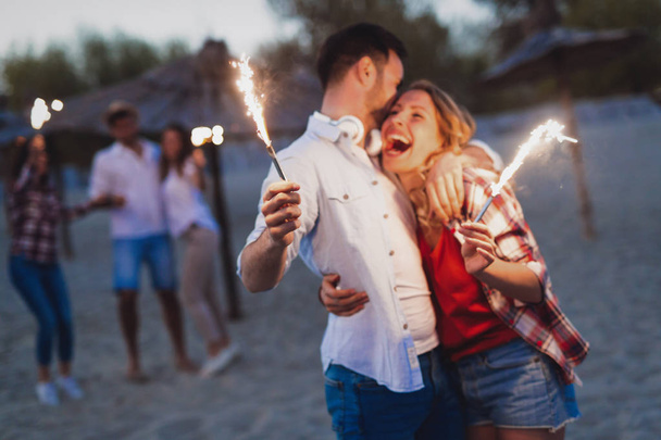Happy group of friends lighting sparklers and enjoying freedom at beach during sunset - Foto, Imagem
