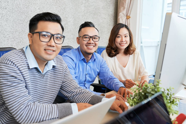 Asian kobieta i mężczyźni siedzący przy pracy biurko z rachmistrz w biuro i uśmiechnięty w kamera  - Zdjęcie, obraz