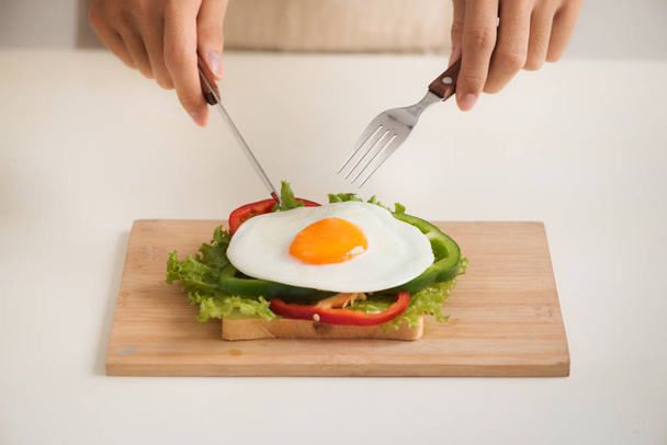 Hands of man cut the eggs on cutting board, served with bread, herbs, sausage and fresh juice. - Foto, Imagem