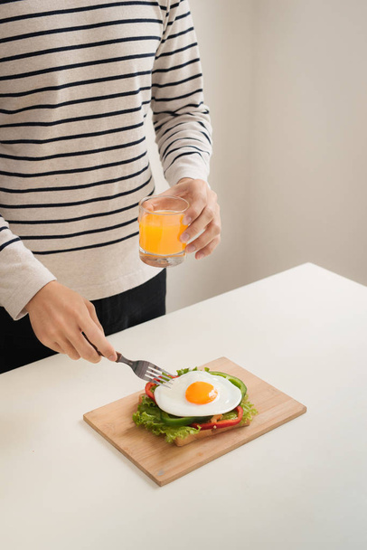 Handen van man snijd de eieren op snijplank, geserveerd met brood, kruiden, worst en vers sap. - Foto, afbeelding