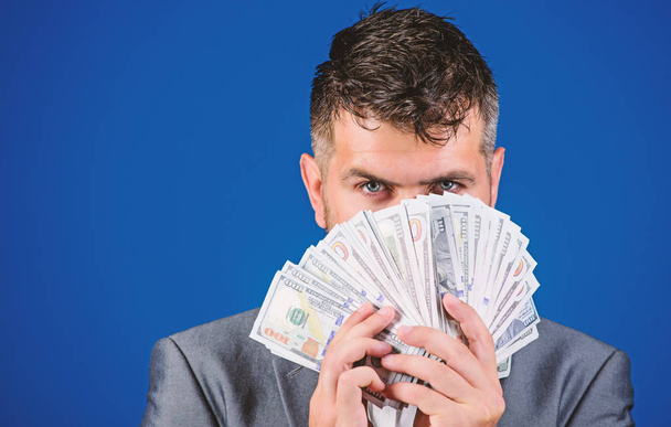 Easy cash loans. Businessman got cash money. Richness and wellbeing concept. Get cash money easy and quickly. Smell of money. Man formal suit hold pile of dollar banknotes blue background - Foto, immagini