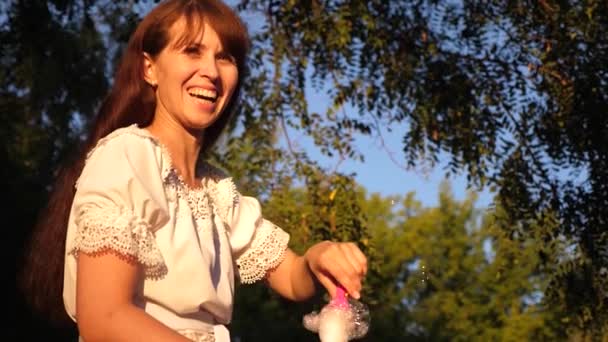 Woman blows big soap bubbles and laughs while walking in park. Summer walks and games in nature - Footage, Video