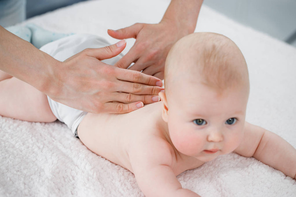 Mother's hands massage the muscles of the back of her baby. - Foto, Bild