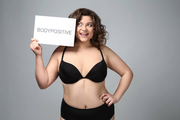 Plus size woman holding paper with text BODYPOSITIVE on grey background - Photo, Image