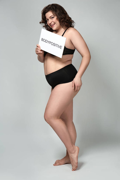 Plus Size Frau hält Papier mit Text-Bodypositiv auf grauem Hintergrund - Foto, Bild