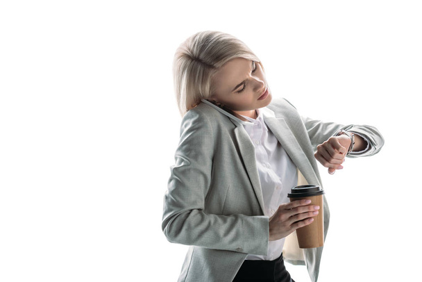 serious businesswoman talking on smartphone, holding paper cup and checking time on watch isolated on white - Φωτογραφία, εικόνα
