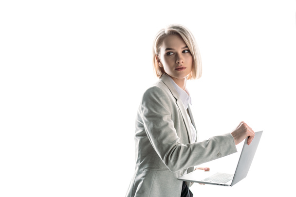 bonita, mujer de negocios confiada sosteniendo el ordenador portátil y mirando hacia otro lado aislado en blanco
 - Foto, Imagen