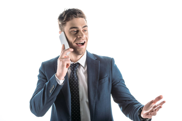 good-looking, cheerful businessman using smartphone and gesturing isolated on white - Foto, Bild